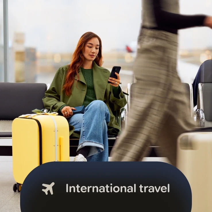 A woman sitting in an airport terminal using her Google Pixel while sitting next to a yellow suitcase, with an overlay reading "International travel" with an airplane icon.