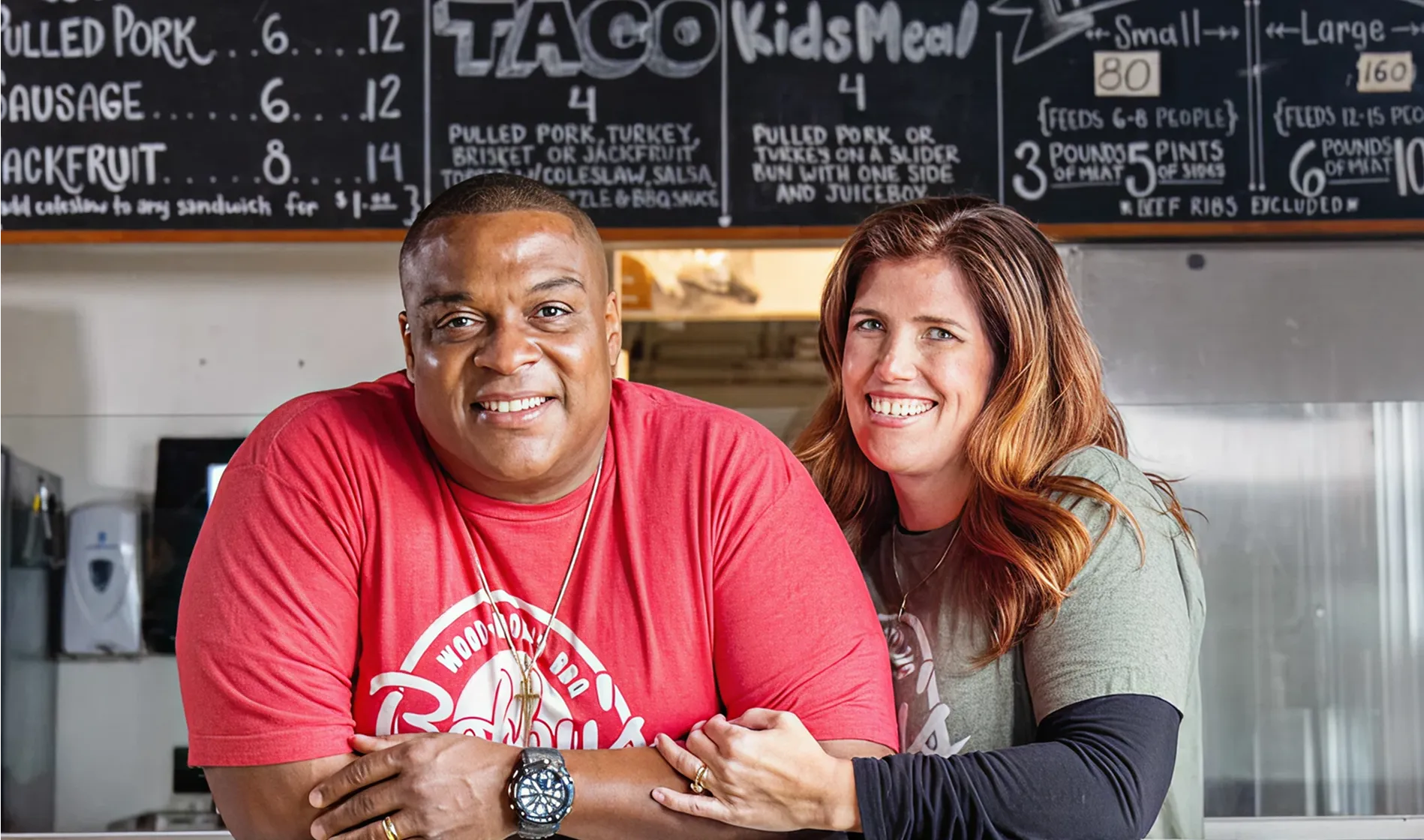 Bobby and his wife proudly stand behind the counter at their BBQ restaurant.